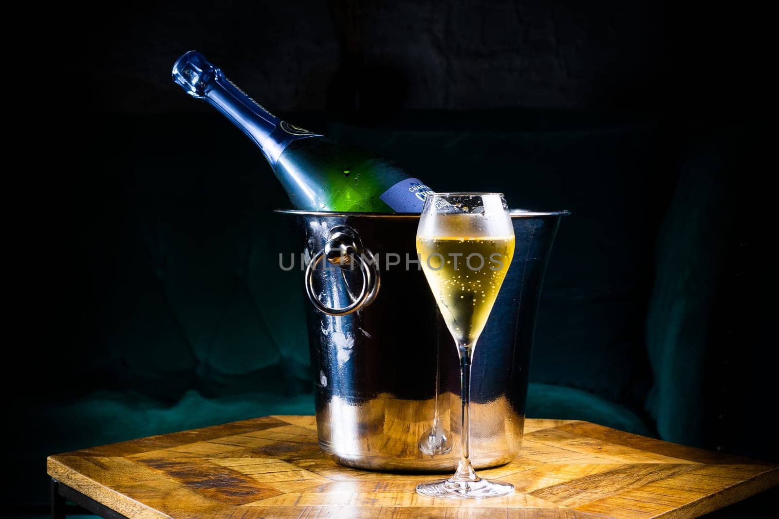 Bottle and cup of champagne on a wooden table, dark background