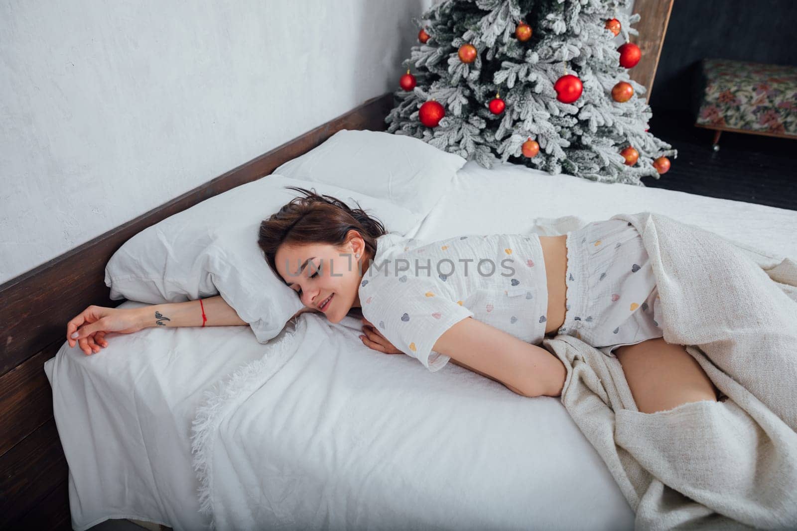 Beautiful woman in pajamas on bed by christmas tree by Simakov