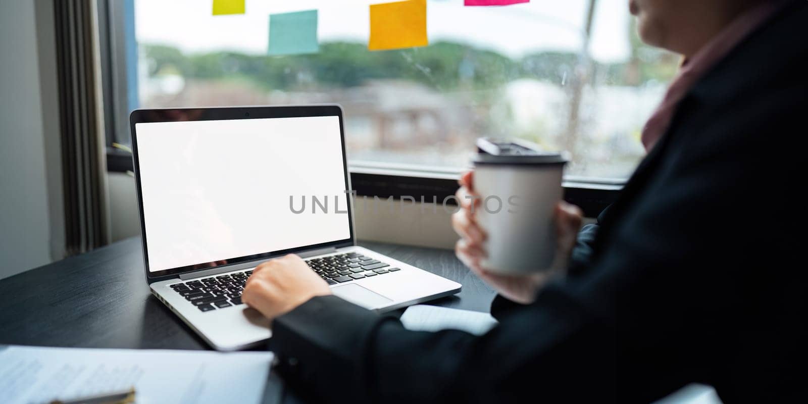 Young Asia businesswoman use laptop with blank white screen mock up display for advertising text while working at her workplace by nateemee