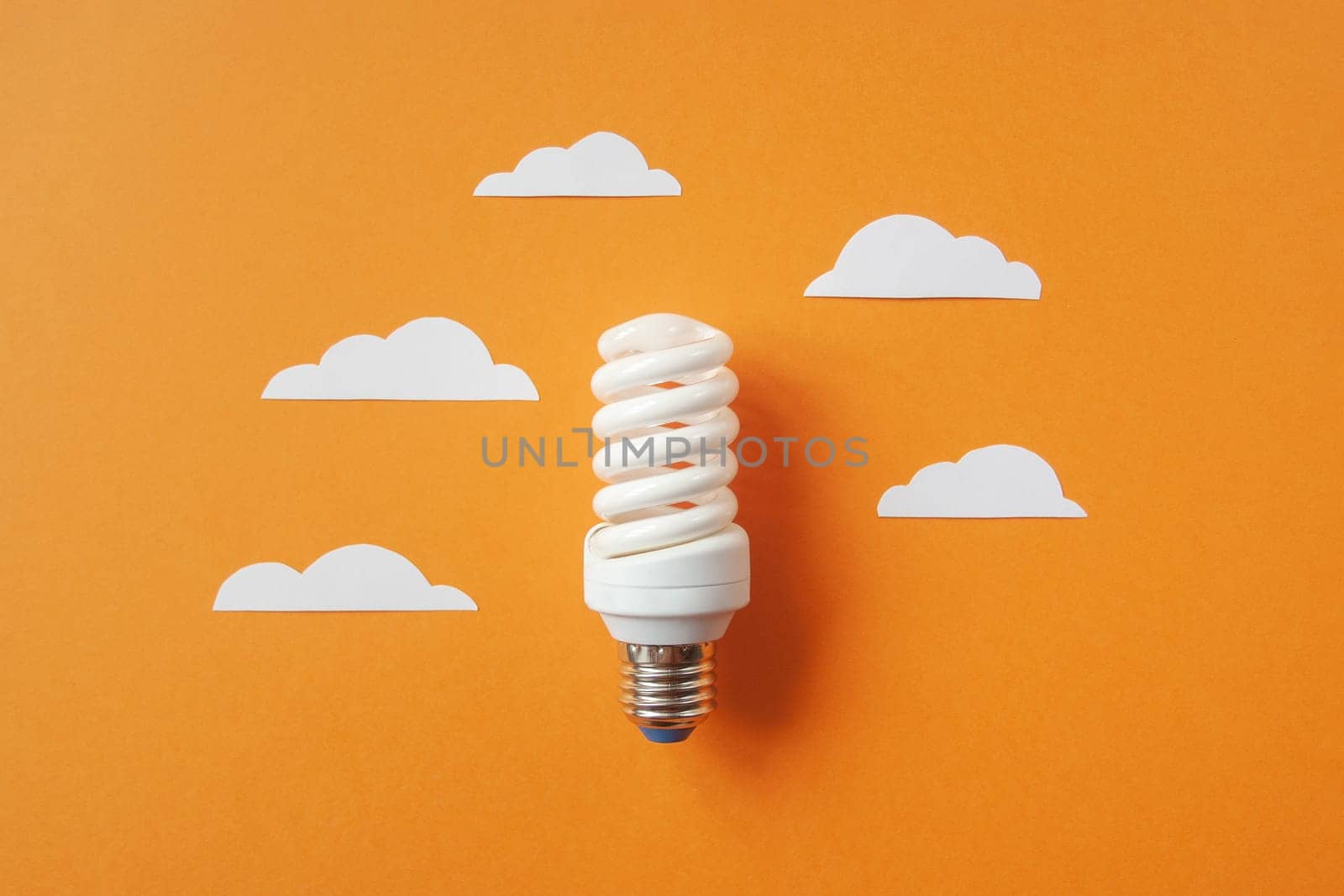 Light bulb with white cut out clouds on orange background. Idea concept. Energy and electricity. alternative energy sources. Innovation and thinking out the box symbols. Creativity and inspiration