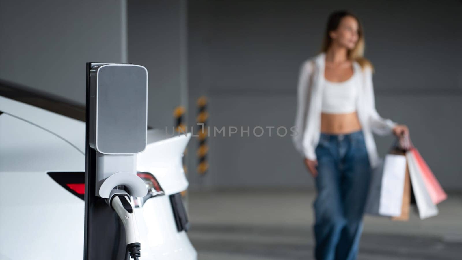 Young woman travel with EV electric car to shopping center parking lot innards by biancoblue