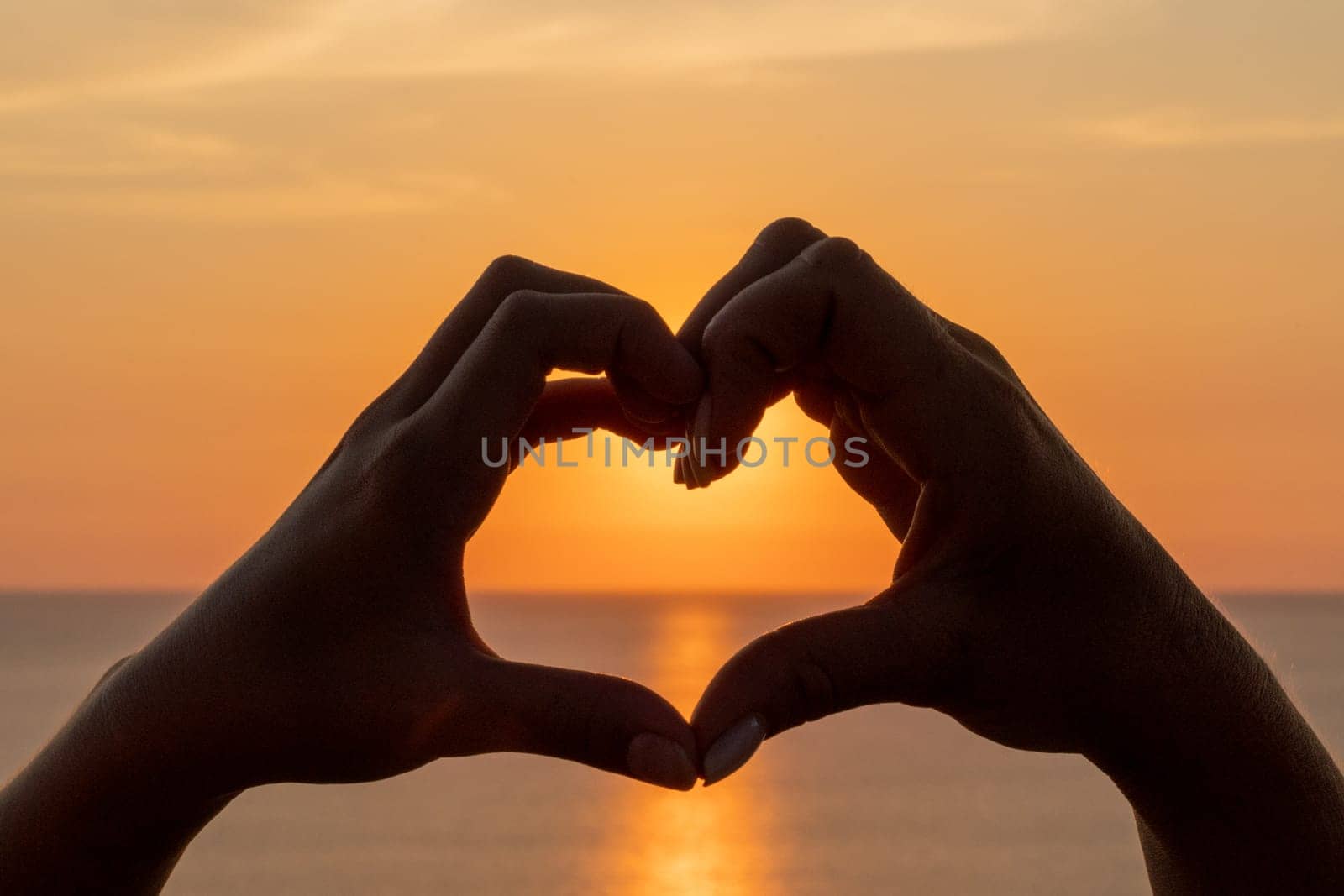 Hands heart sea sanset. The image features a beautiful sunset with two people holding their hands up in the air, forming a heart shape. by Matiunina