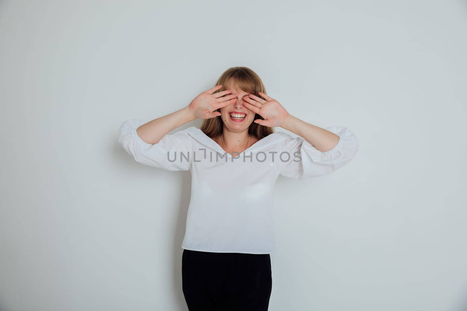 A woman closes her eyes with her hands against a light background