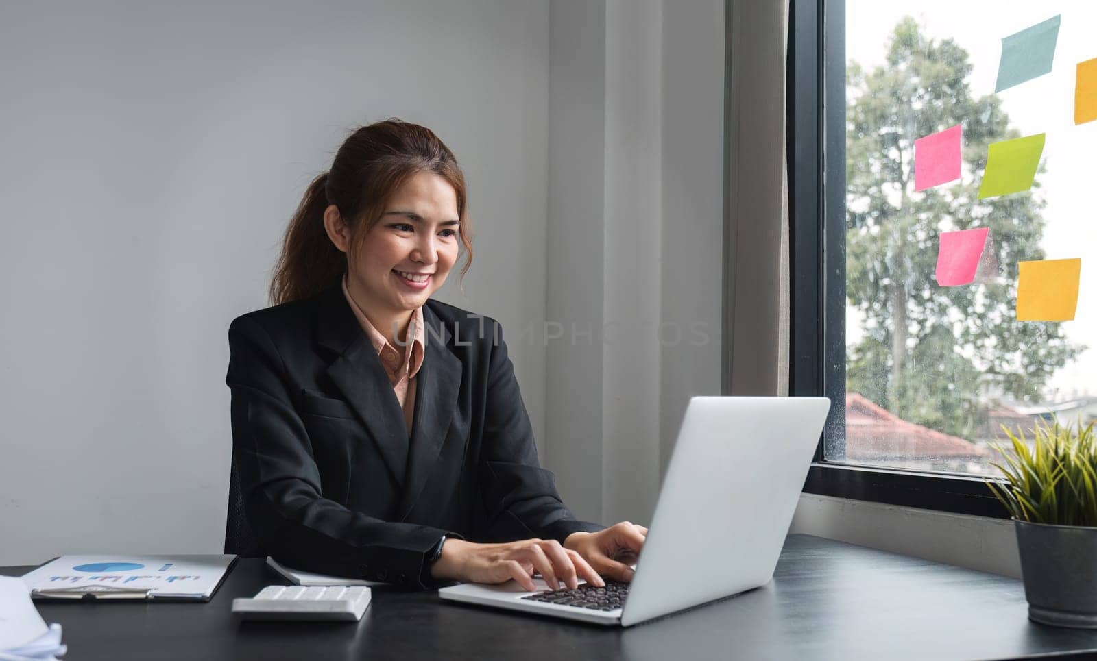 Professional Asian business woman intent on work focusing on laptop in modern office by wichayada