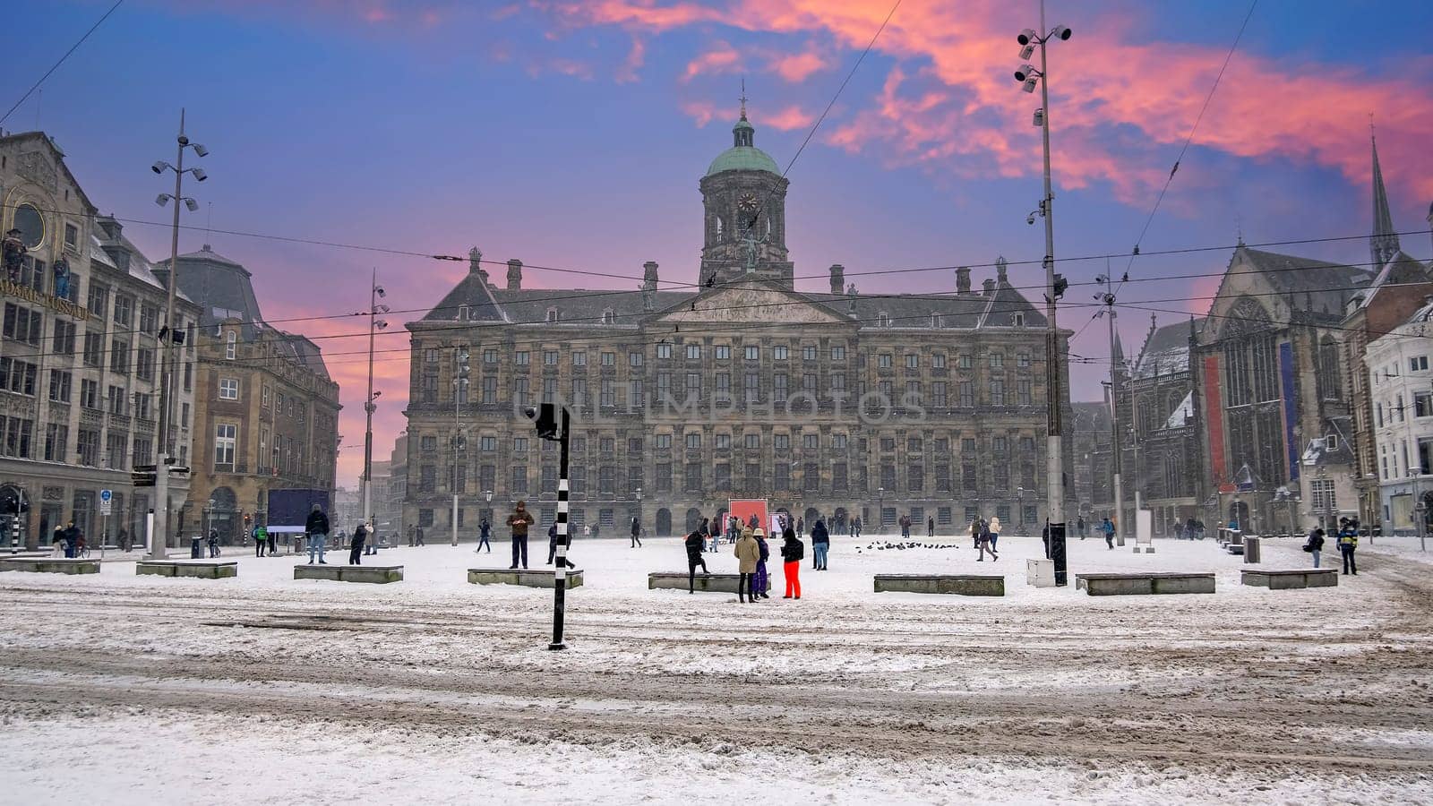 Snowy city Amsterdam at the Dam square in the Netherlands in winter at sunset