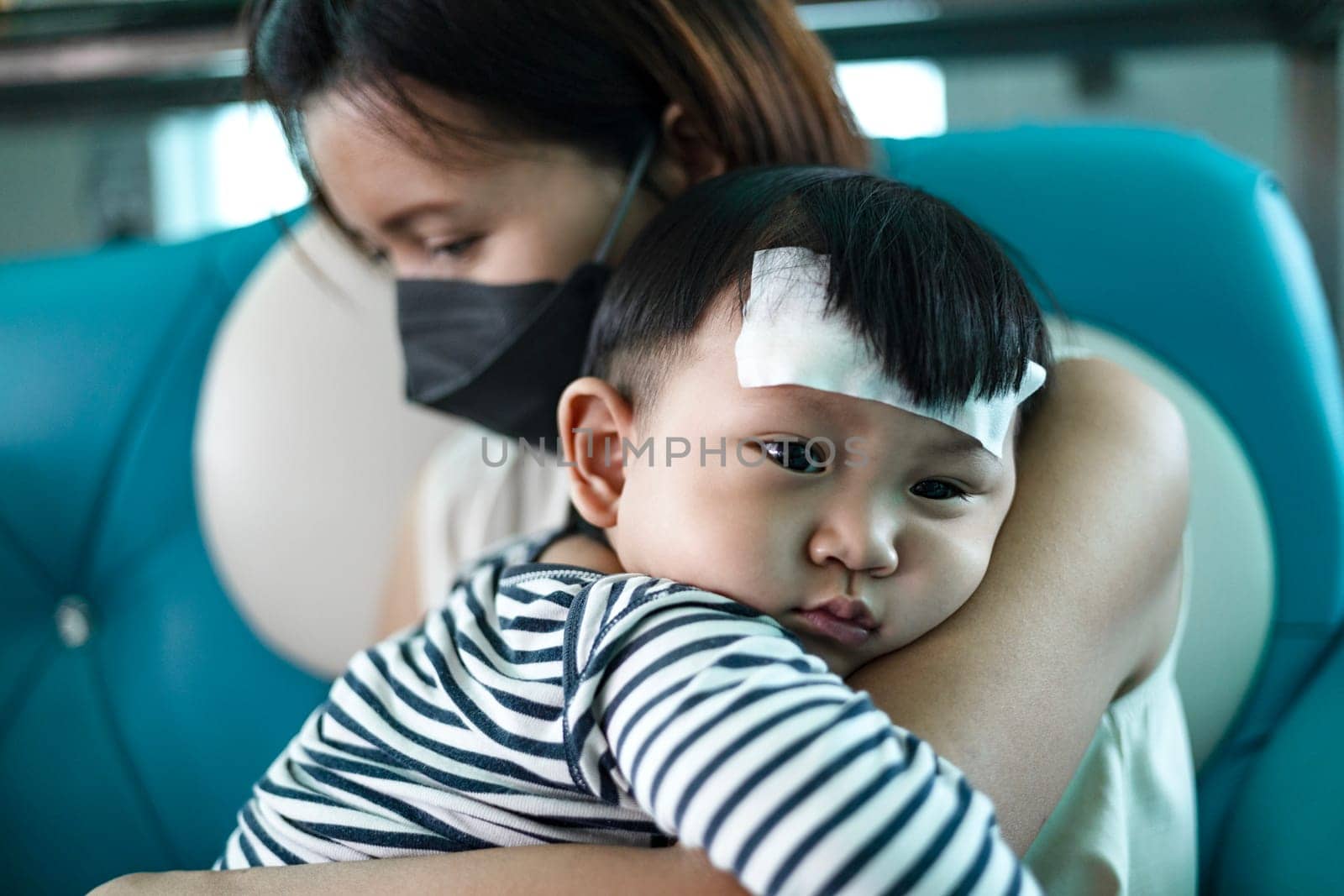 Mother attach cooling fever patch gel for reduce temperature her son. A little boy who is not feeling well on his Mother shoulder.