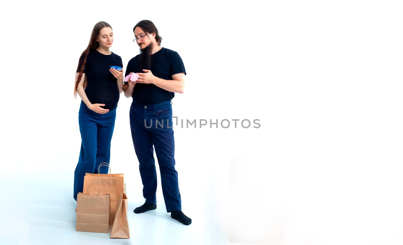 young pregnant woman and her husband with shopping bags andchoose blue for a boy or pink for a girl on white background. Pregnancy shopping concept happy young family with shopping bags