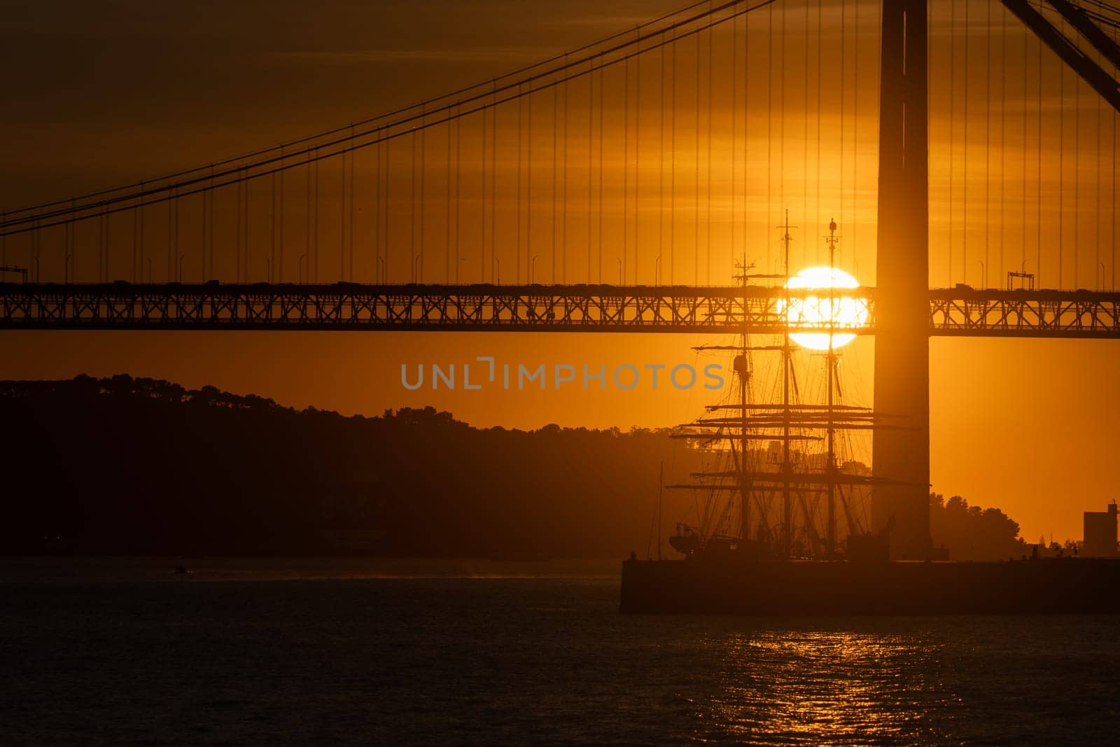 The sun is setting behind a large bridge