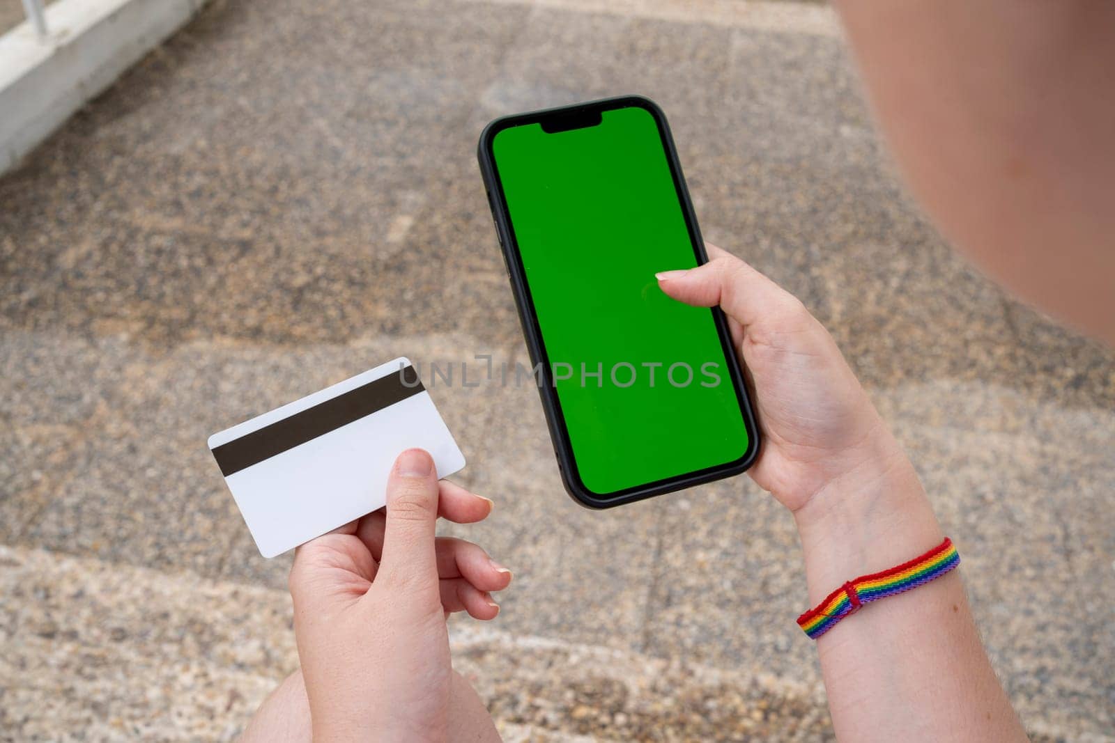 From above of anonymous young female in sneakers with rainbow hand band sitting on marble steps with chromakey screen mobile phone and checking information while browsing messages....