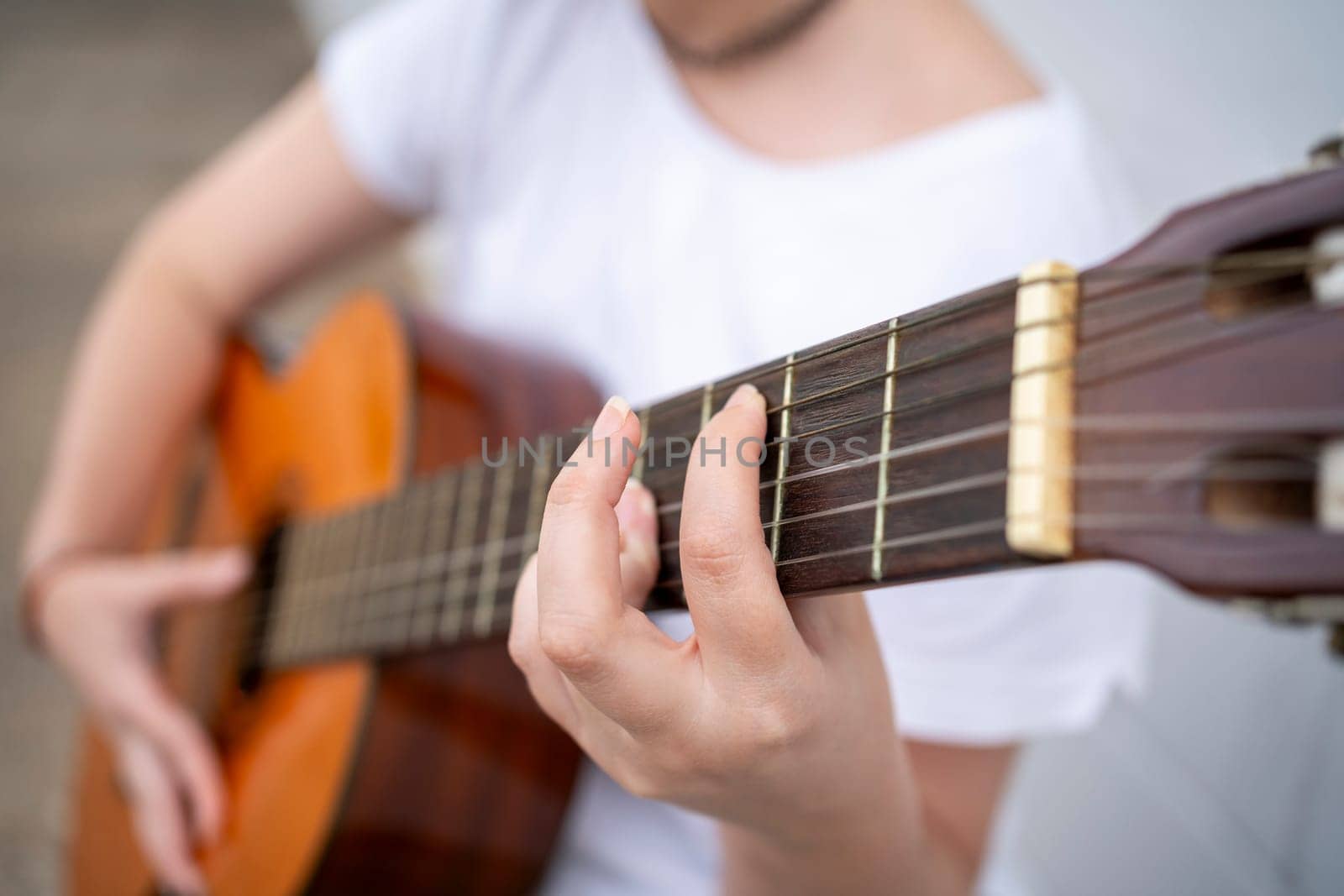Soft focus of crop anonymous female guitarist playing acoustic guitar on city street during performance on summer day