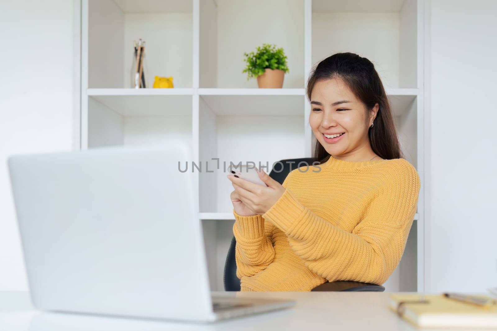 Young woman sitting in front of computer laptop and using mobile phone.