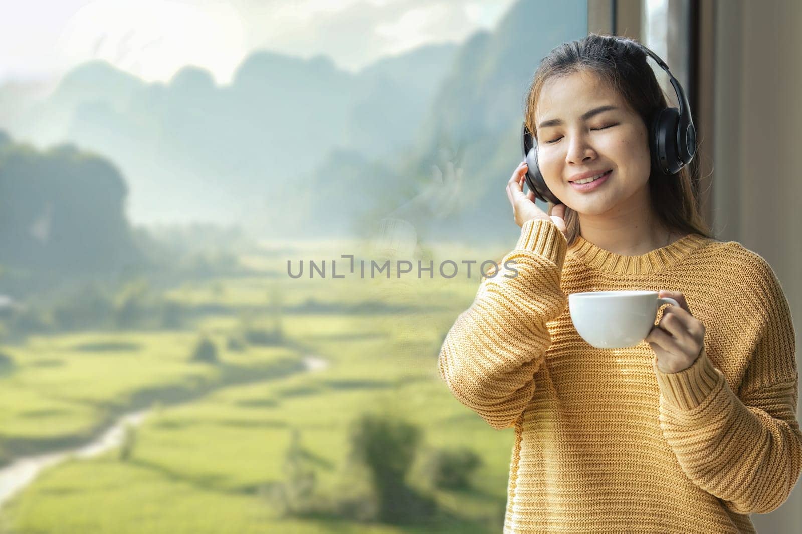 Young woman standing at the window she listening to music with headphones and looking at the view in the bedroom at resort.