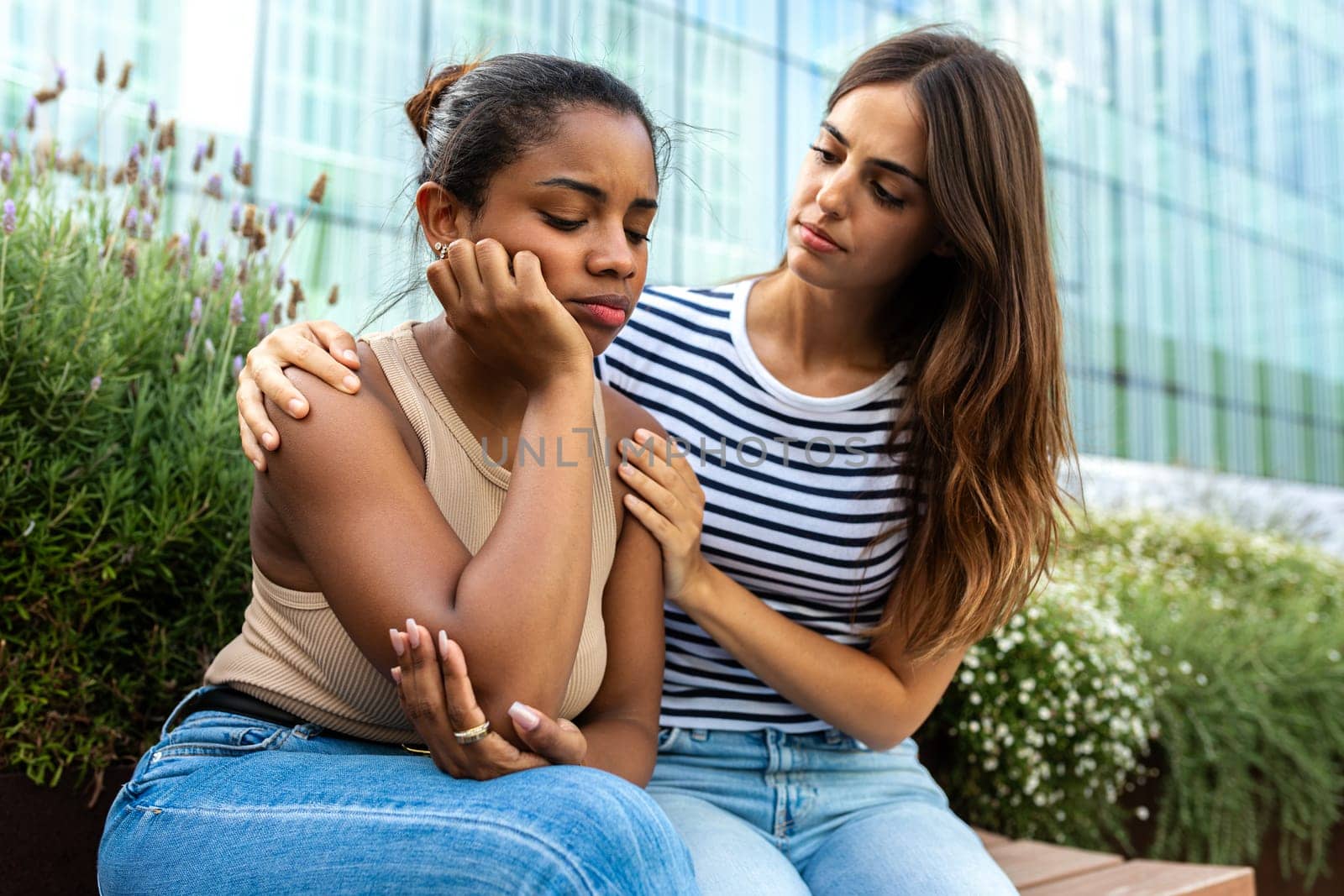 Young woman consoling and comforting upset and depressed African American female friend in park outdoors. Friendship concept.