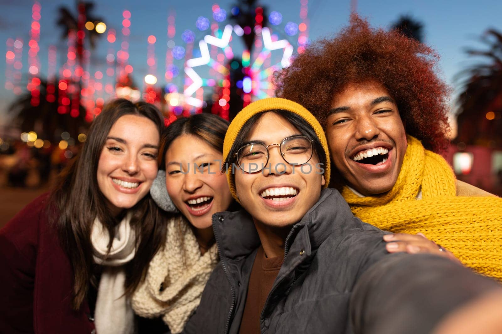Multiracial young friends laughing and having fun together taking selfie during winter Christmas market looking at camera. Friendship concept.