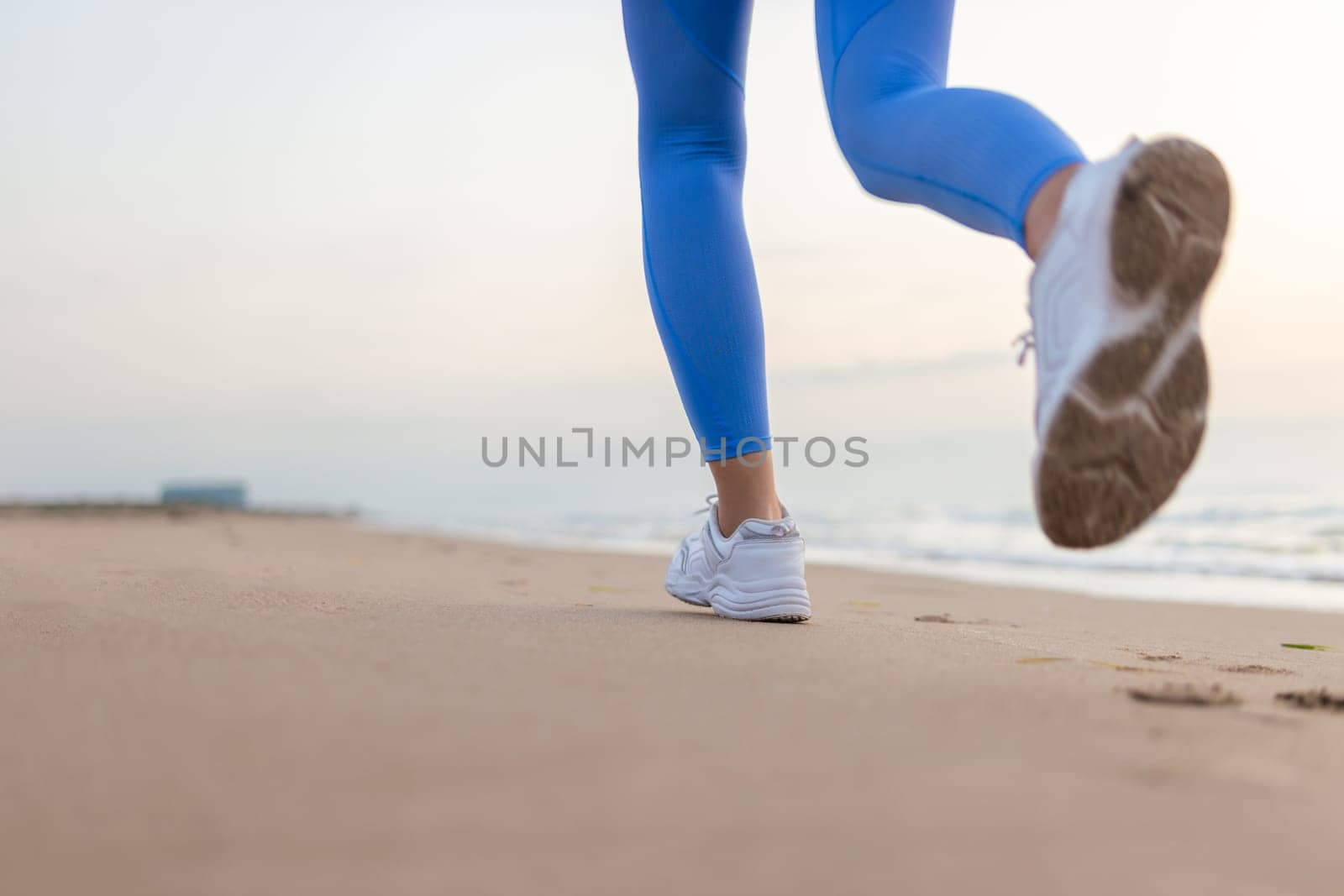 legs of a girl in blue leggings and sneakers running along the beach at dawn with space for inscription. High quality photo