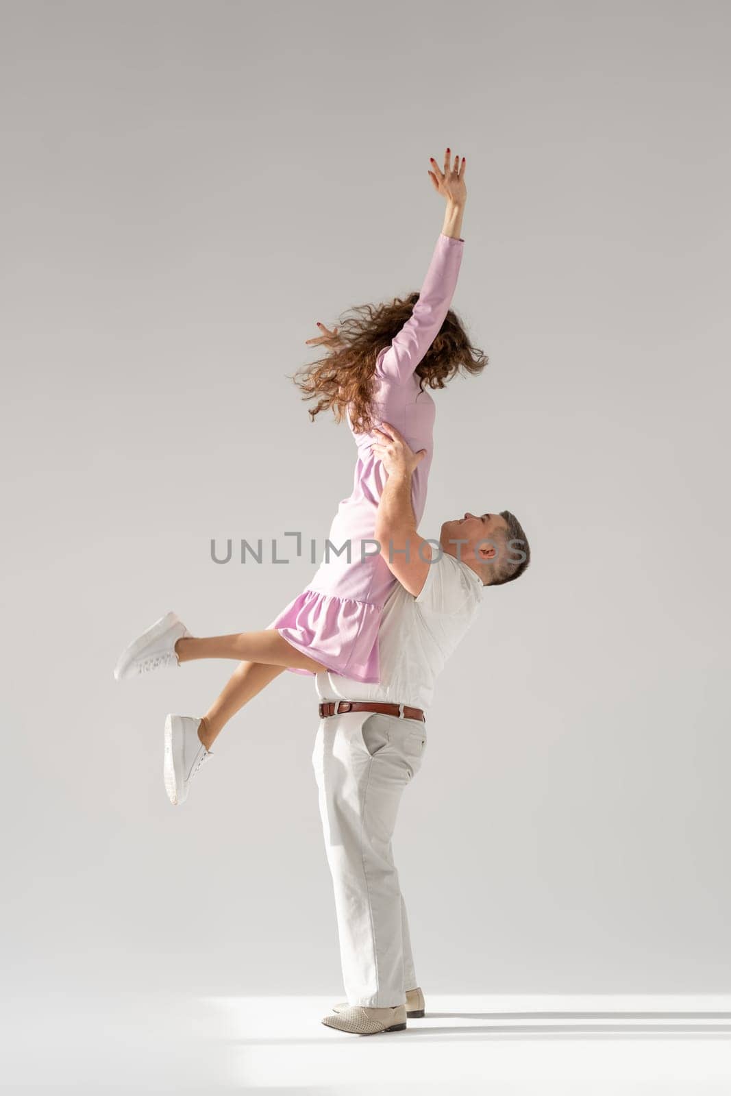 Beautiful young couple dancing on light background. Full length of young beautiful couple bonding while standing against white background