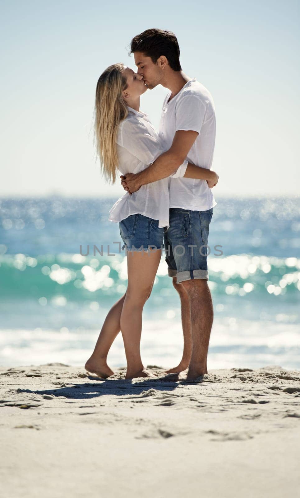 Couple, beach kiss and hug with love, support and care on a date by the sea with romance on vacation. Holiday, ocean and outdoor with summer travel in nature relax on a break and trip by the water by YuriArcurs