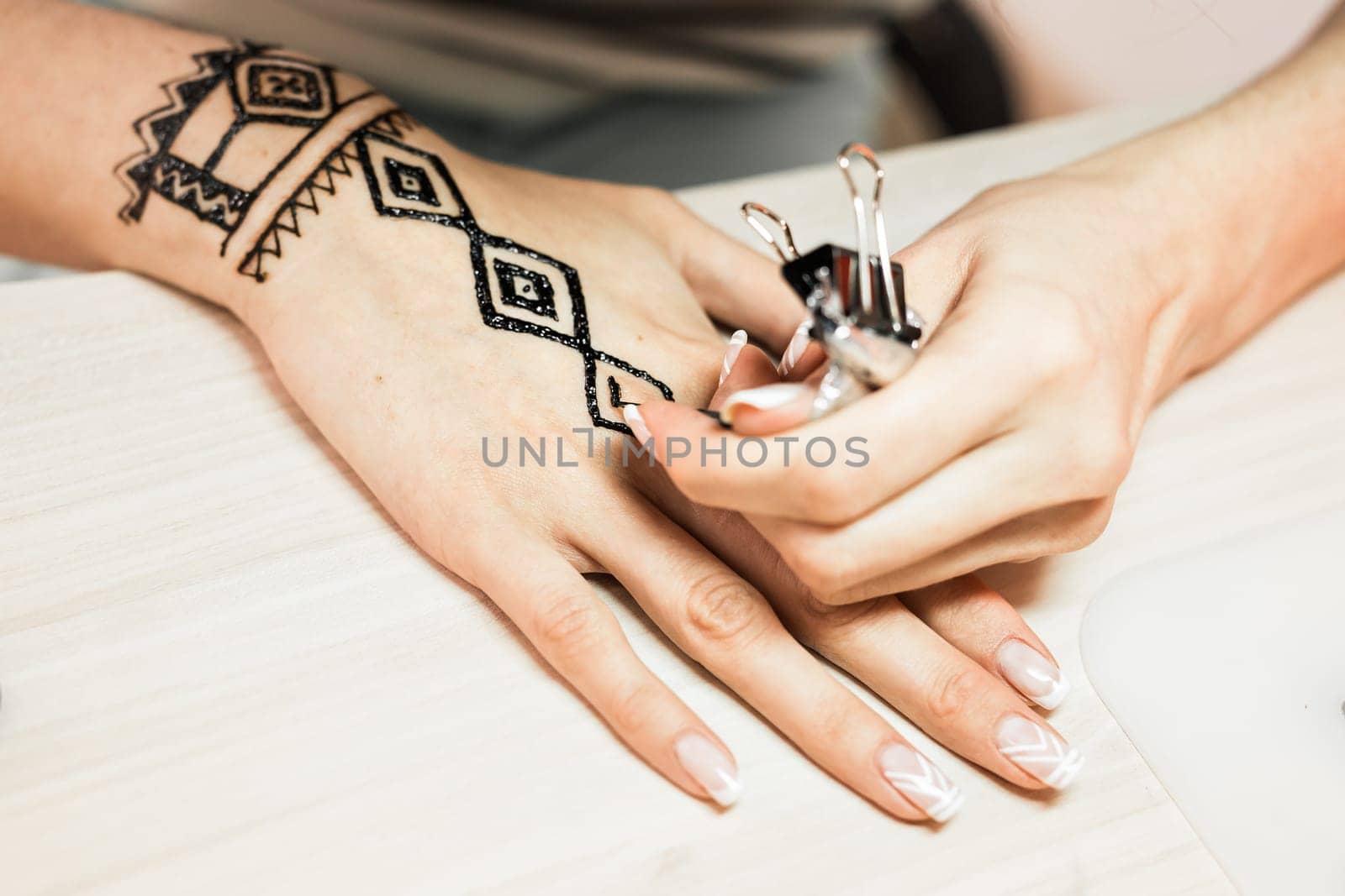 young woman mehendi artist painting henna on the hand.