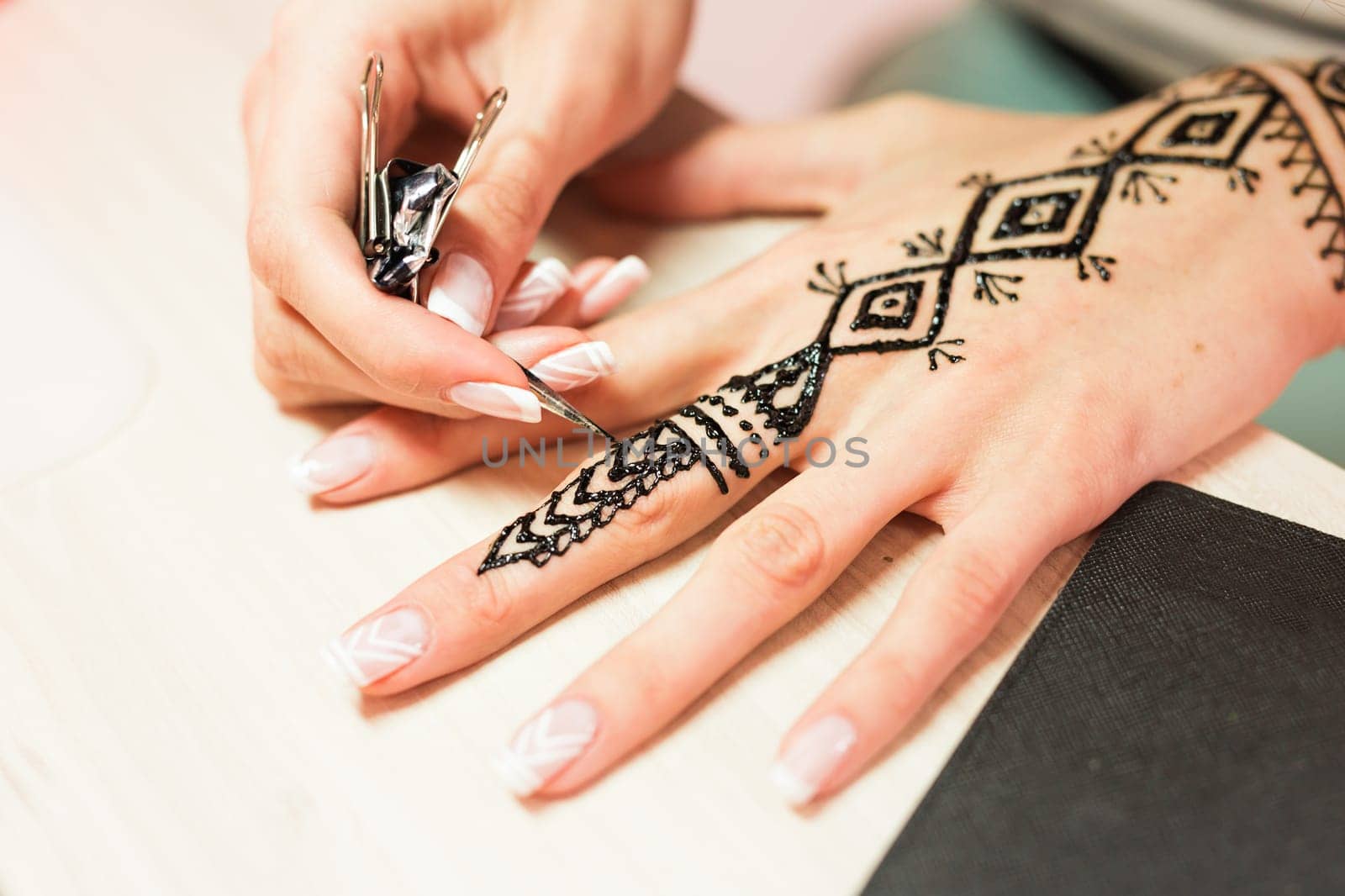 young woman mehendi artist painting henna on the hand.