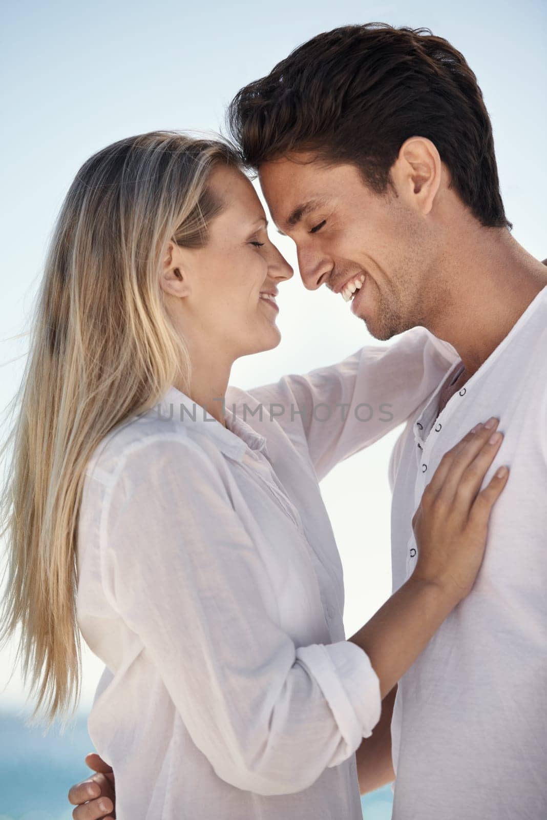 Couple, beach and laugh with hug with love, support and care on a date by the sea with romance on vacation. Holiday, ocean and outdoor with summer travel in nature relax on a break and trip by water.