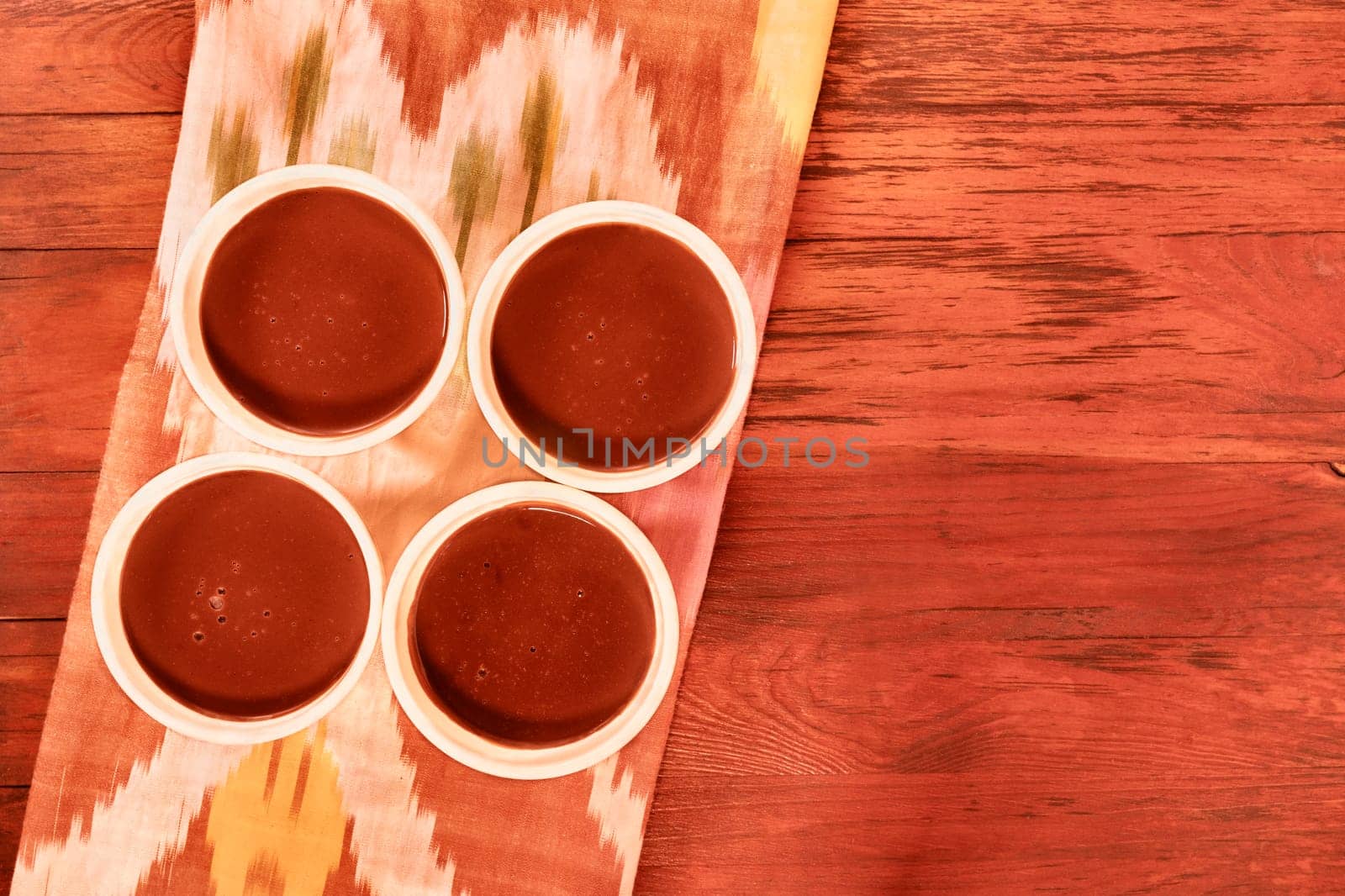 Four bowls with chocolate pudding on red wooden table