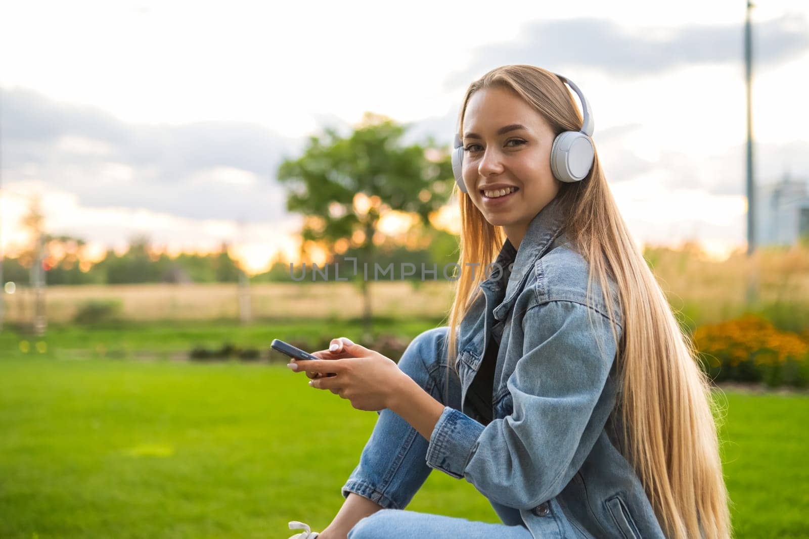 Portrait of the young woman spending free time in the park at sunset