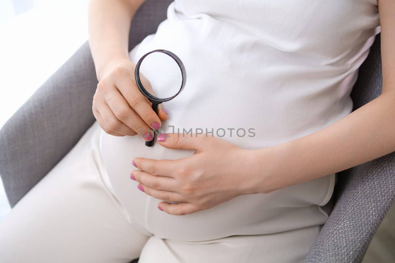 Pregnant woman holding a magnifying glass near her belly.