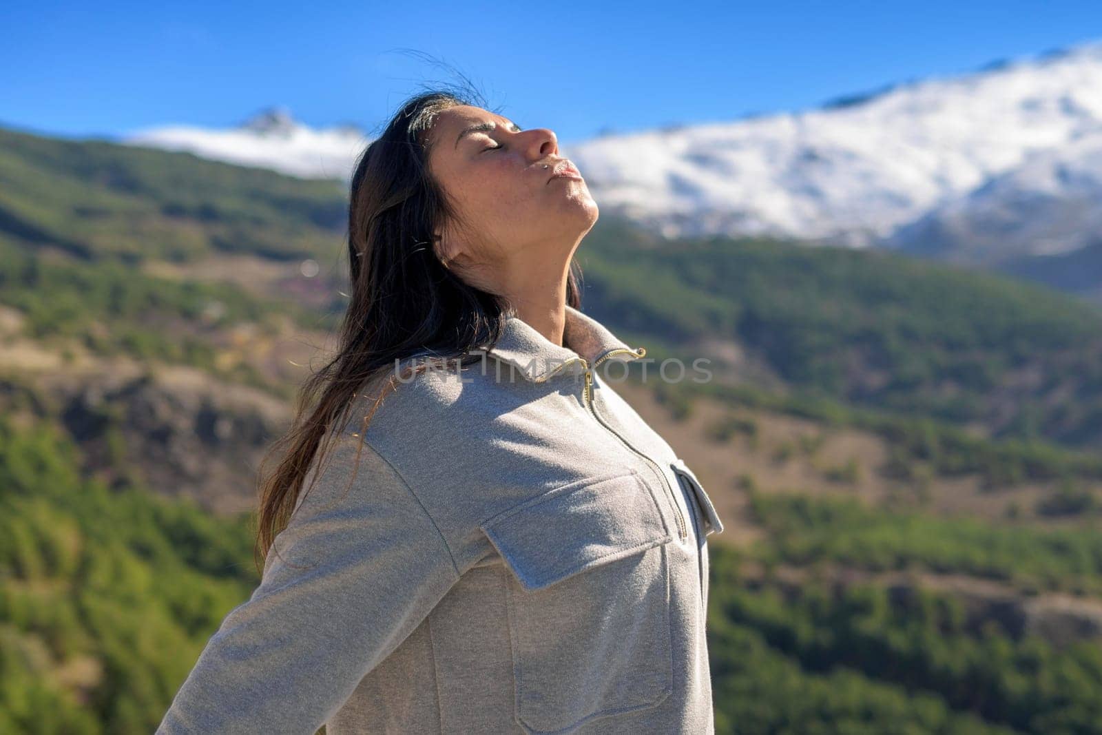 beautiful middle-aged latina woman, arms stretched back, breathing deeply, with the sun in front of her, high in the peaks of sierra nevada, granada.,