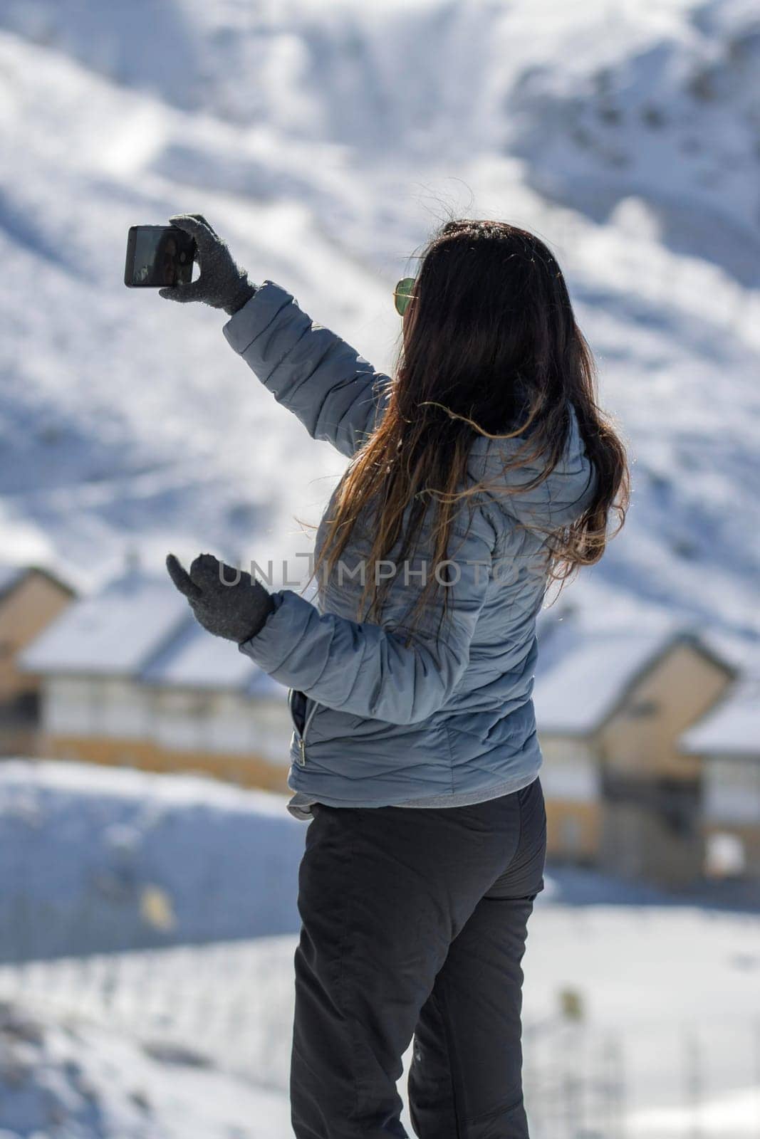 middle-aged latina woman taking a selfie in the mountains of sierra nevada, in the ski resort of granada, with her smart phone