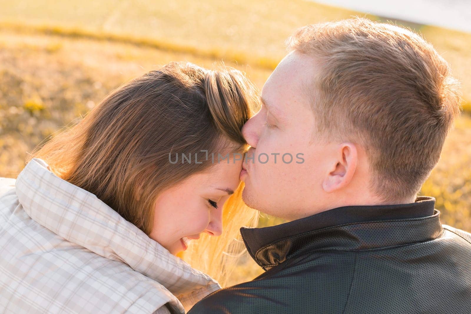 Sweet kiss. Handsome young man kissing his girlfriend on forehead in autumn park by Satura86