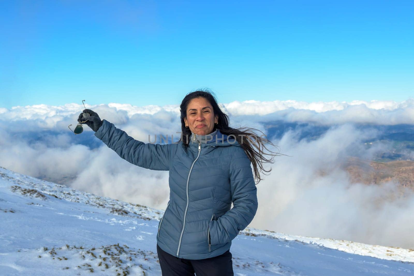 portrait of latin woman smiling in the snow, with warm clothes above the clouds, on the top of the mountain of sierra nevada