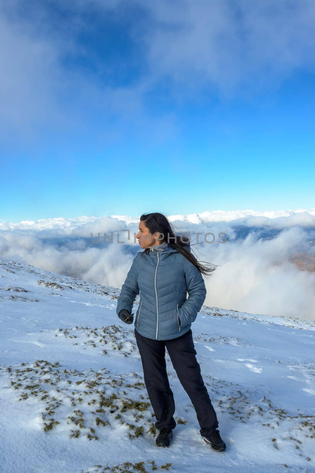 middle-aged latina woman on a snow-capped mountain above the clouds,