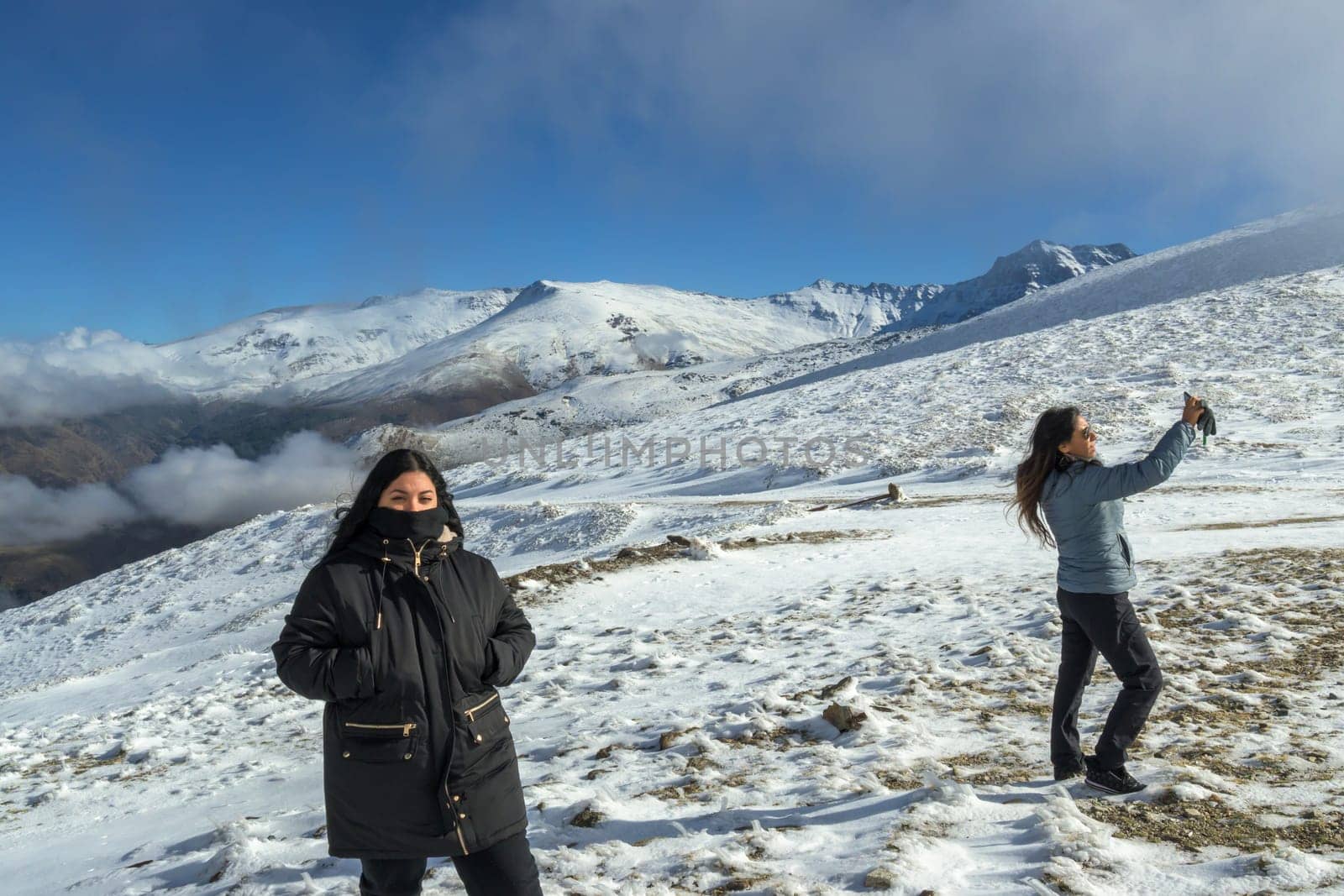 two Latin women enjoy a winter day in sierra nevada,granada, taking a selfie with a smartphone. by carlosviv