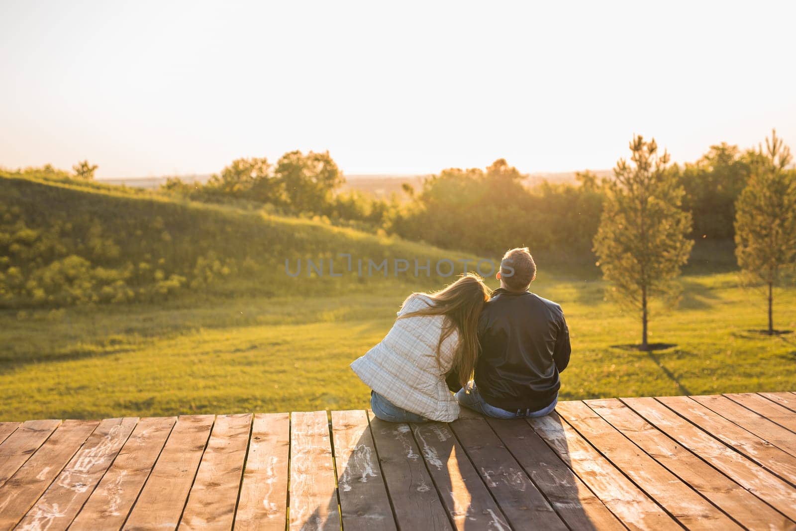 Romantic young couple enjoying a date sitting in a close embrace on a park bench overlooking a lake, view from behind