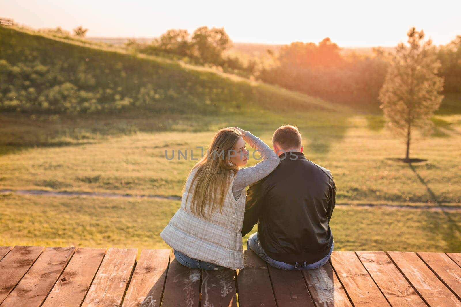 Romantic young couple enjoying autumn nature sitting in a close embrace, view from behind by Satura86
