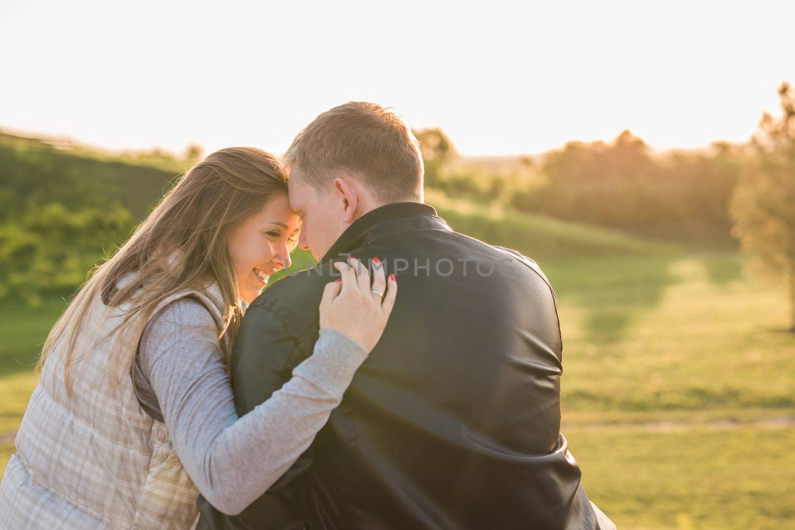 Romantic young couple enjoying a date sitting in a close embrace on a park bench overlooking a lake, view from behind