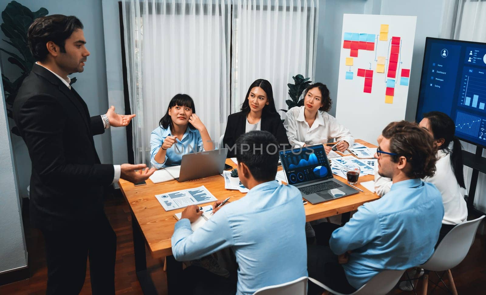 Diverse group of business analyst team analyzing financial data report. Finance data analysis chart and graph dashboard show on TV screen in meeting room for strategic marketing planning. Habiliment