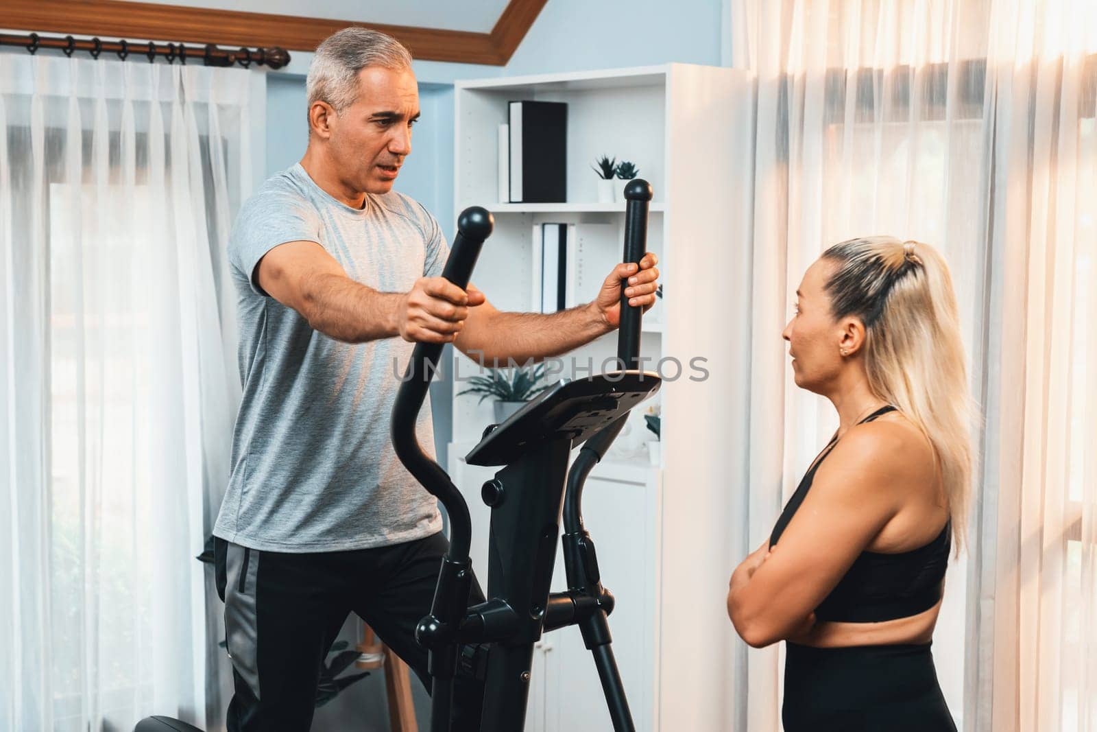 Active senior couple running on elliptical running machine at home together as fitness healthy lifestyle and body care after retirement for pensioner. Clout
