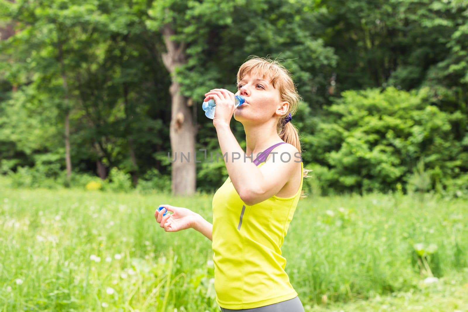 Fitness woman drinking water after work out exercising on summer outdoor portrait.