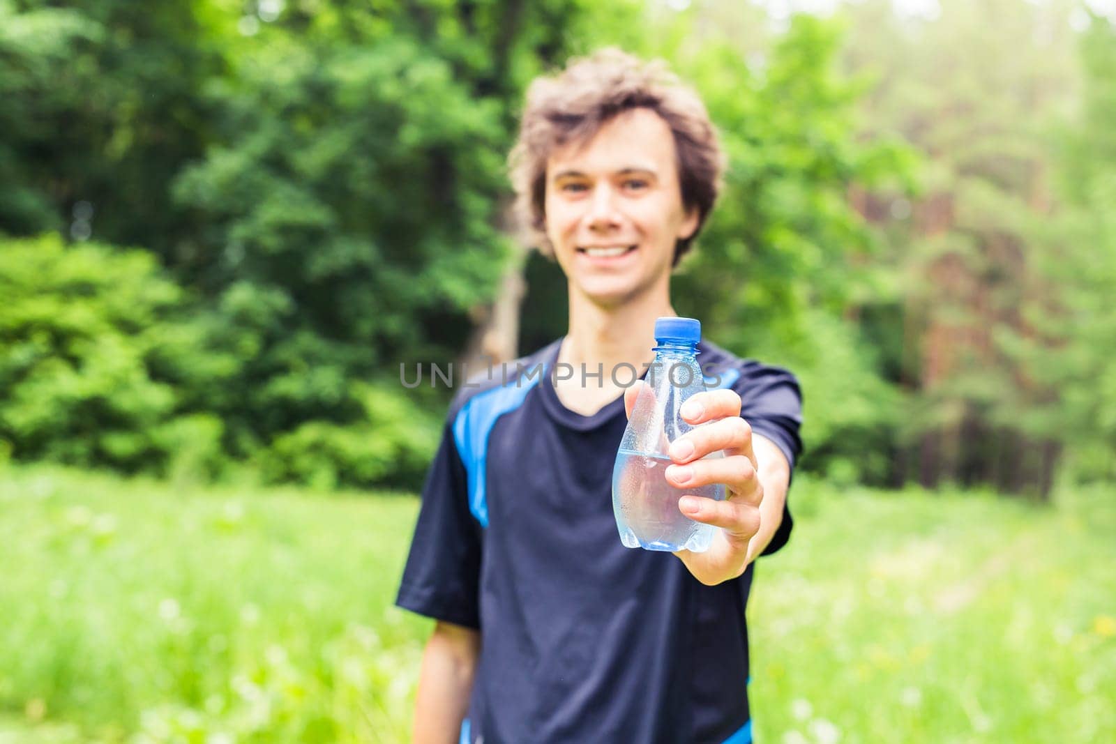 Sportsman with a bottle of water after running outdoors in park.