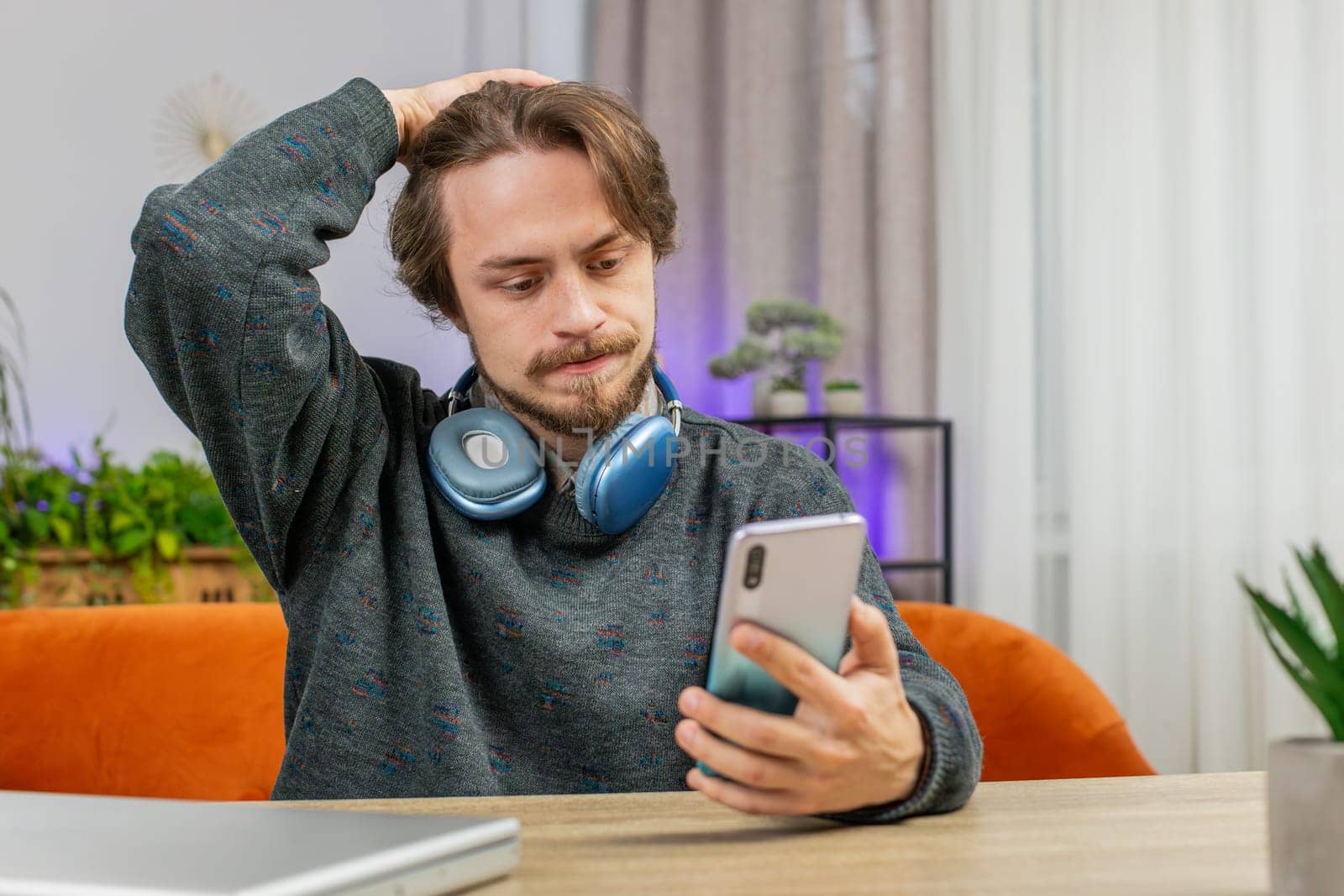 Sad displeased Caucasian man use smartphone typing browsing, loses becoming surprised sudden lottery game results, bad news, fortune loss fail, deadline, virus. Young adult guy at home office at table