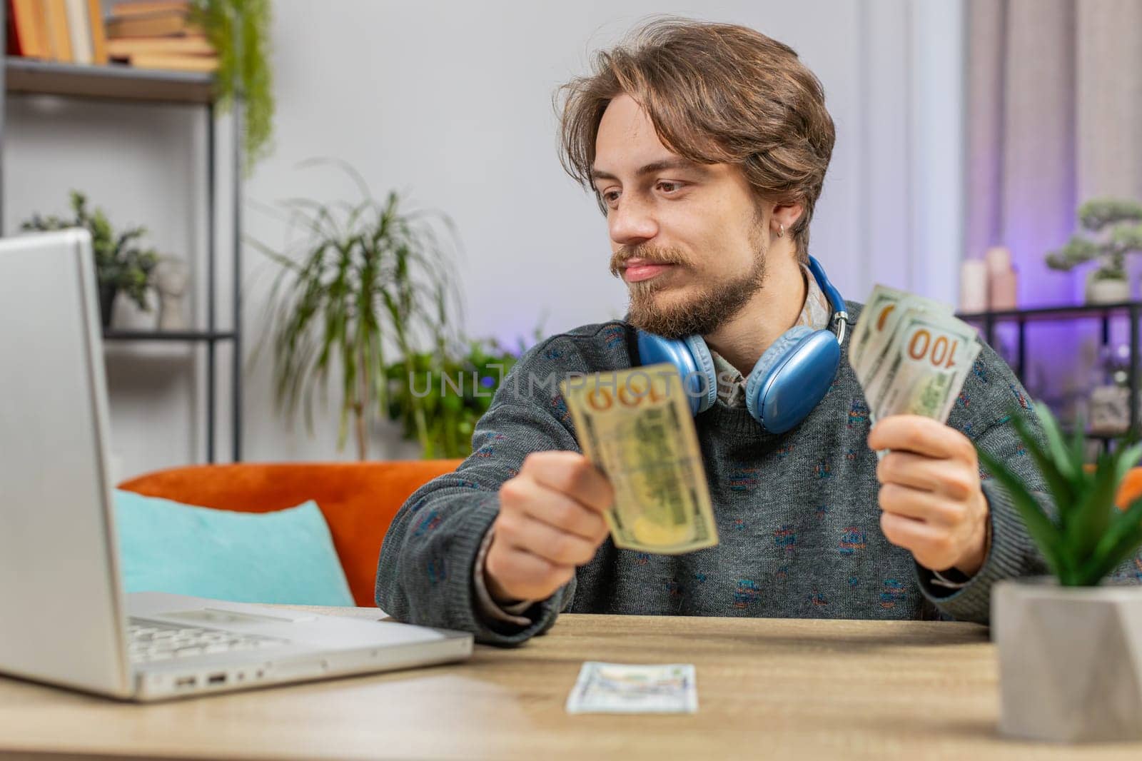 Planning budget. Rich happy man counting money cash use laptop computer calculate domestic bills at home table. Freelancer guy satisfied of income salary earnings, money for planned vacation gifts
