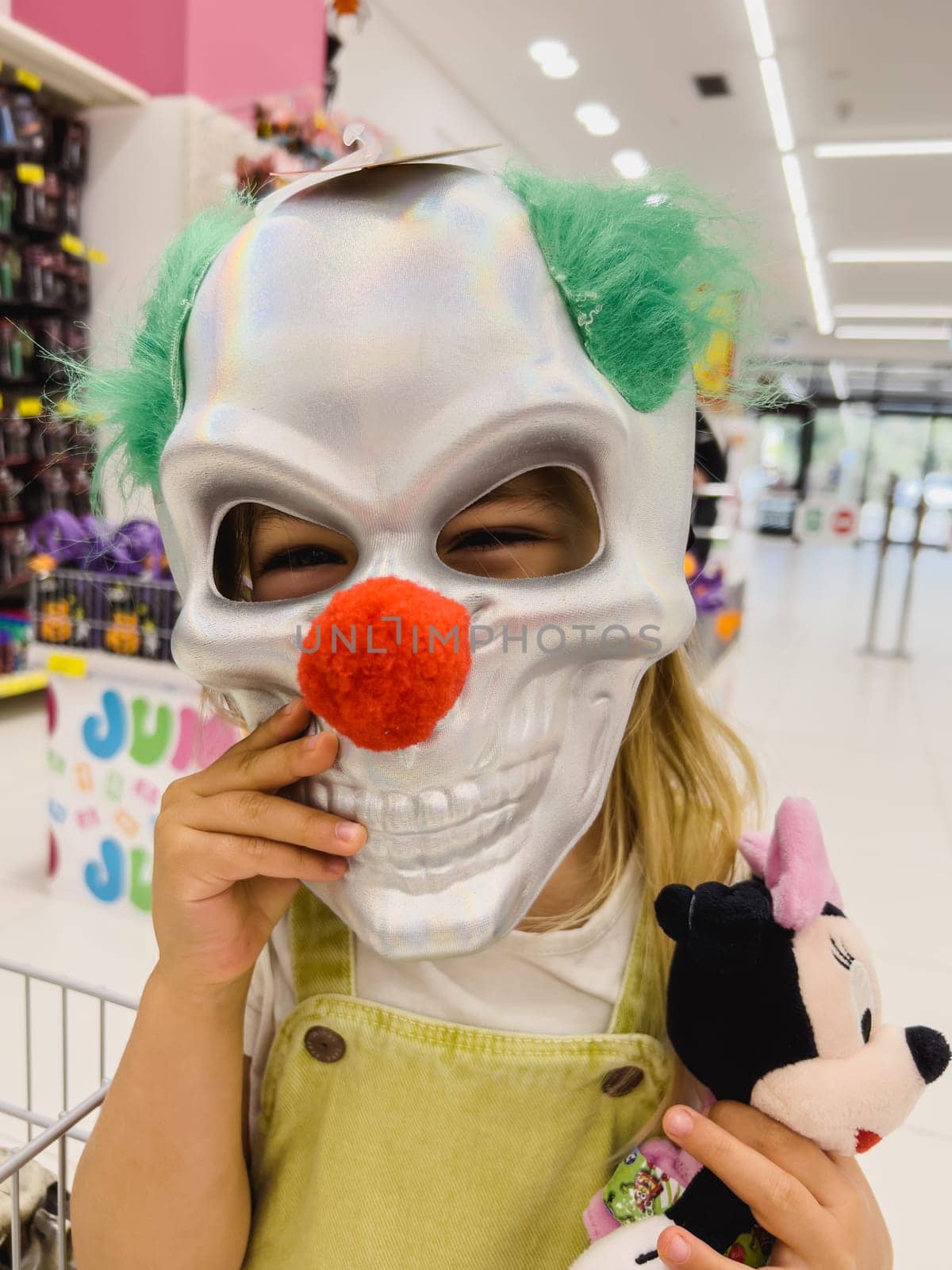 Little girl in the store trying on a scary clown mask. High quality photo