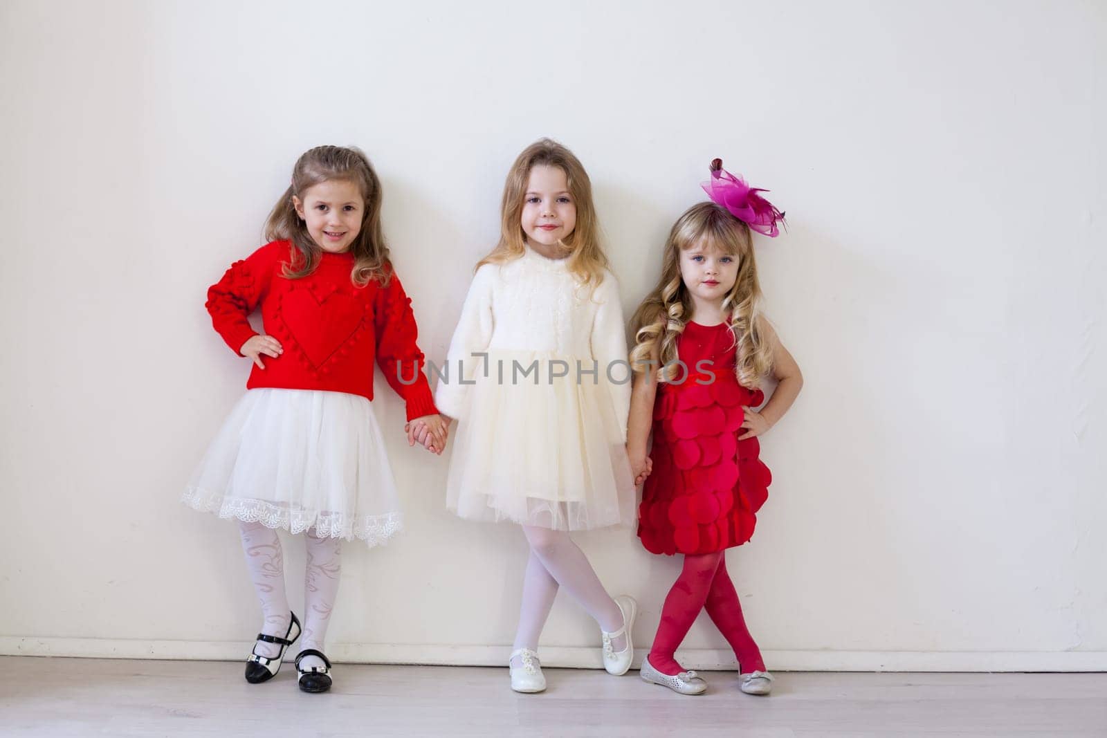 Three little beautiful girls in red hold hands by Simakov