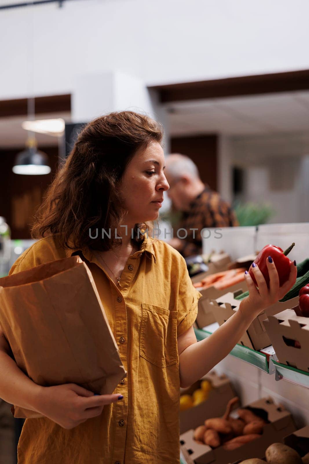 Woman in zero waste shop purchasing farm grown vegetables, picking ripe bell peppers. Client in plastic free local grocery shop looking to buy nutritious food, using decomposable paper bag