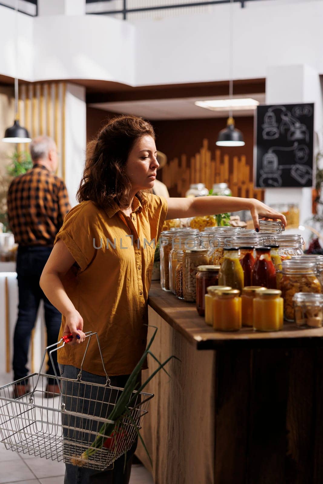 Woman holding shopping basket, buying ecofriendly bulk products in zero waste store designed to minimize plastic usage. Green living customer looking for nutritious groceries