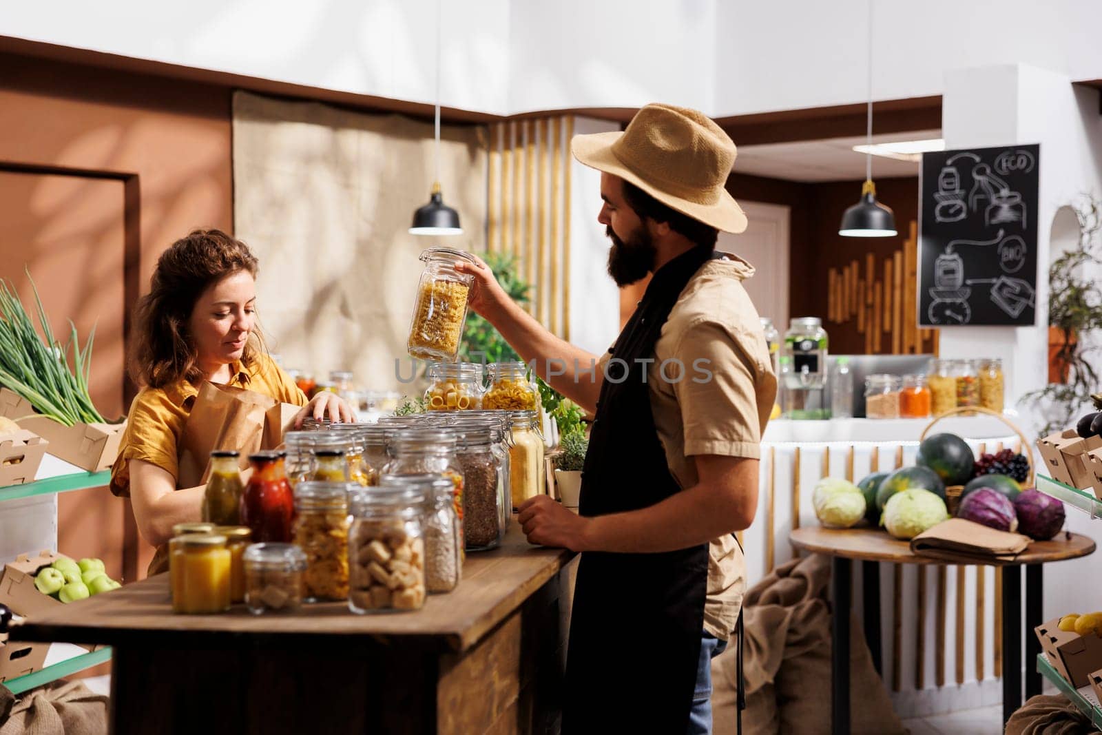 Client shopping for pantry staples in environmentally conscious zero waste store, being assisted with advice by trader. Merchant showing woman ecological nonpolluting products