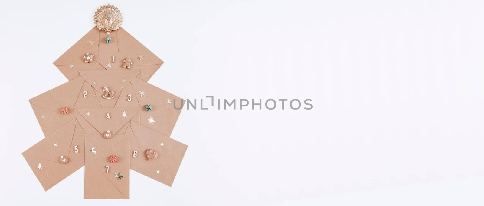 Creative Christmas advent calendar made from craft envelopes, wooden numbers, cookies and Christmas decor on the left against white background with space for text on the right, top view close-up.