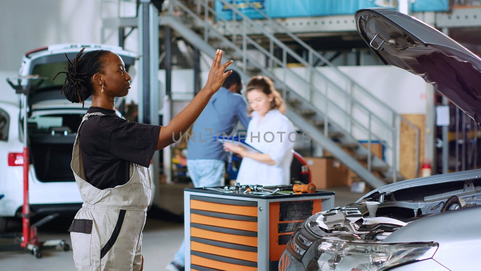 Licensed engineer in auto repair shop using augmented reality hologram to visualize car components in order to fix them. African american woman using AR technology while working on damaged vehicle