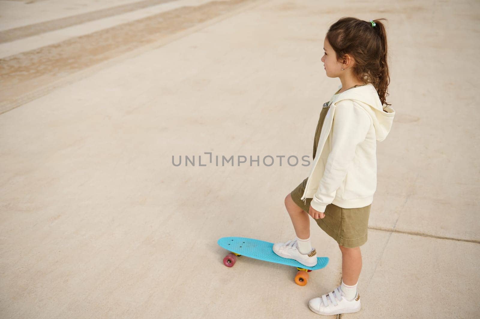 Overhead view of Caucasian little child girl looking away while playing skateboard, or surf skate and start on outdoor pump track in skatepark by extreme sports. People. Childhood. Leisure activity